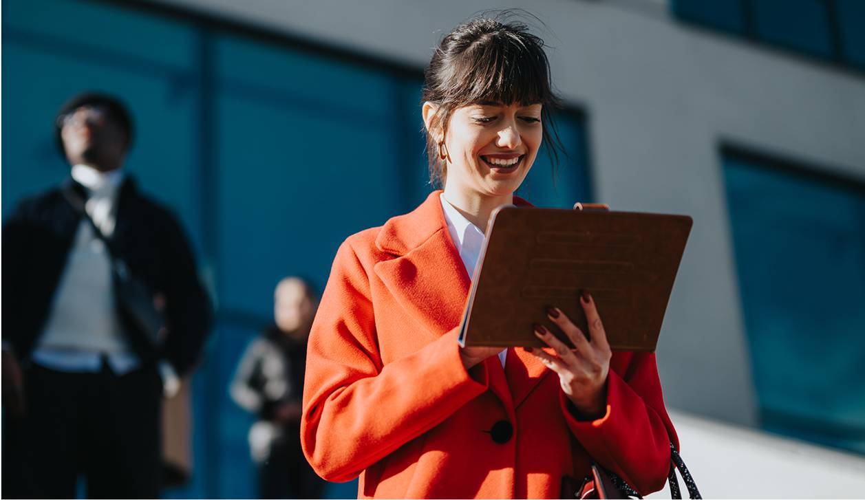 Woman in orange coat using tablet outside office-rectangle