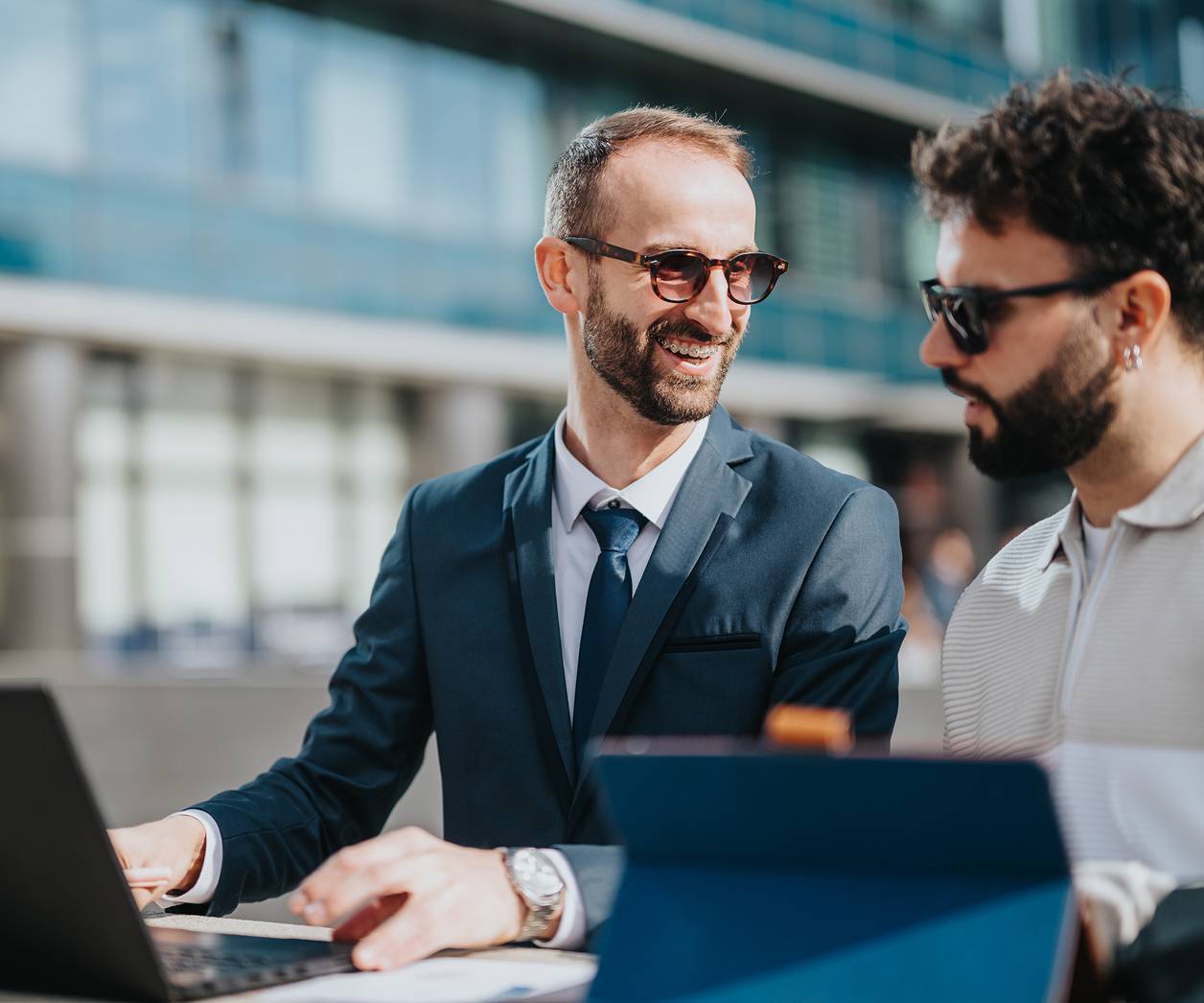 Two business people collaborating outside with laptop and tablet
